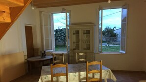 A dining area with a table set for four, two chairs, a cabinet, and a window with a view of trees and a fence. - Superb gîte in the Bordeaux countryside (Saint-Vivien-de-Blaye)