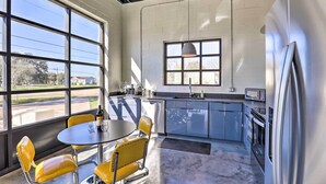 Una cocina moderna con ventanas amplias, una zona de comedor con sillas amarillas y electrodomésticos de acero inoxidable.