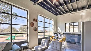 Una habitación amplia con ventanas grandes, un sofá, dos sillones, una mesita y una zona de cocina con refrigerador y fregadero.
