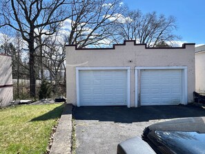 Eine Garage mit zwei weißen Türen, einer Betonauffahrt und einem Rasenstück mit Bäumen.