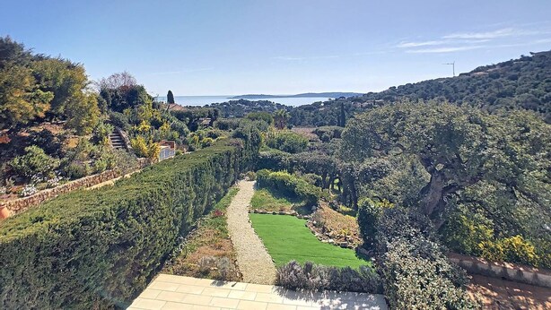 A landscaped garden with a pathway leading to a green lawn, surrounded by dense vegetation and hills in the background. - In estate with swimming pool, tennis, club house, house for 6 people, sea view (SAINTE MAXIME)