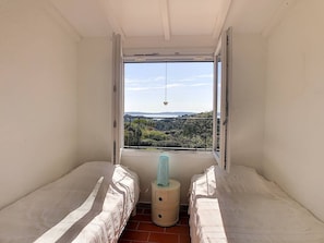 A small room with two beds, a window with a view of a landscape, and a small table with a lamp.
