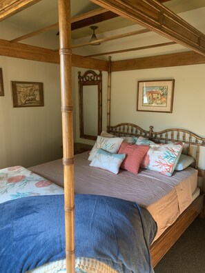 Una cama con dosel y tablero de madera, un espejo grande y dos cuadros en la pared.