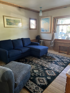 Una sala de estar con un sofá seccional azul, un tapete estampado y piso de madera.
