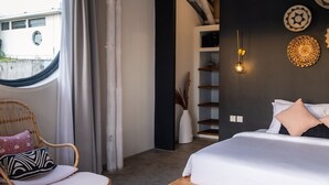 Un dormitorio con una cama, una silla de mimbre, un ventanal redondo y una pared decorada con platos.