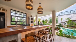 Una cocina moderna con un ventanal grande, taburetes de madera y vista a una piscina.