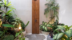 Una puerta de madera con pomo circular, rodeada de plantas en macetas y un camino de piedra.