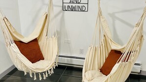 Two beige hammocks with brown pillows in a room with a tiled floor and a wall-mounted sign that reads "RELAX AND UNWIND". - Modern Luxury! Central Downtown Condo with parking! (License #6072) (Estes Park)