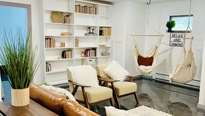 A modern living room with a glass coffee table, leather sofas, a white bookshelf, and two macramé hammocks. - Modern Luxury! Central Downtown Condo with parking! (License #6072) (Estes Park)