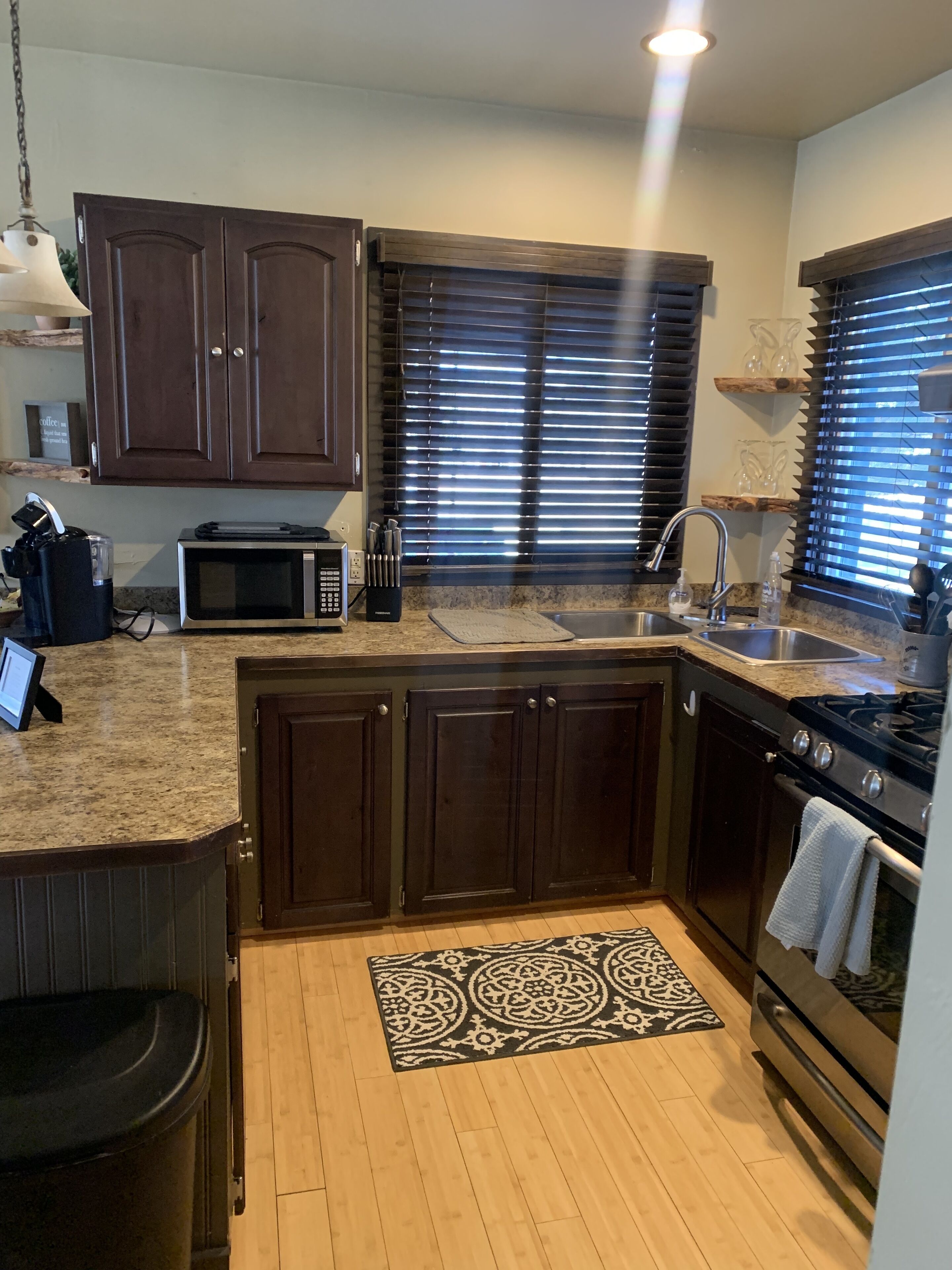 A modern kitchen with dark wooden cabinets, a built-in microwave, a stainless steel sink, and a gas stove.