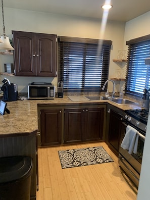 A modern kitchen with dark wooden cabinets, a built-in microwave, a stainless steel sink, and a gas stove.