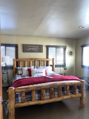 A wooden-framed bed with a plaid bedspread and pillows, a red throw blanket, and a wall with a motivational quote.
