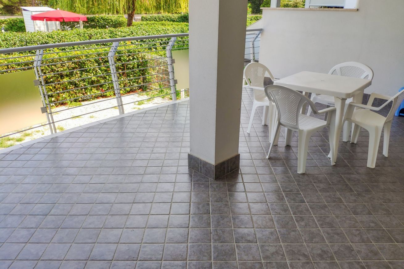 A covered outdoor area with a tiled floor, a white table with chairs, and a view of a garden and water feature.