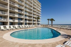 Un espace piscine d’hôtel avec une piscine à l’eau cristalline, des chaises longues blanches et un bâtiment doté de balcons.