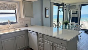 Une cuisine dotée d’un grand îlot central, d’un évier et d’un lave-vaisselle. La fenêtre offre une vue sur la plage.
