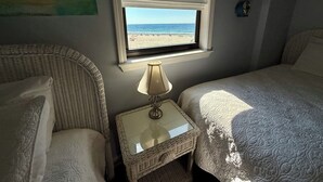 Une chambre avec deux lits, une fenêtre donnant sur la plage, une lampe sur une table de chevet et une carte accrochée au mur.