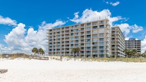 Un hôtel à plusieurs étages doté de balcons, situé sur une plage bordée de palmiers, sous un ciel dégagé.