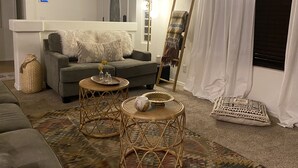 A living room with a grey sofa, a small round table, a woven basket, and a patterned rug.