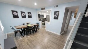 Una cocina moderna con armarios blancos, un microondas y una estufa. Hay un comedor con una mesa y sillas de madera.
