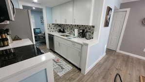 Una cocina compacta con armarios blancos, estufa negra y salpicadero de azulejos.