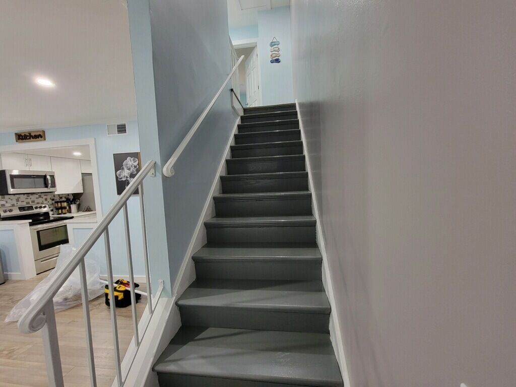 En trappa leder upp till ett köksområde med vita skåp och en mikrovågsugn.