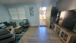 Una sala de estar con sofá, mesa de centro y mueble para televisión. Hay una puerta que da a un espacio exterior.