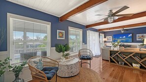 A living room with a ceiling fan, large windows with blinds, a television, and a bookshelf.