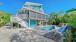 A modern two-story house with a swimming pool, outdoor seating, and a covered patio area. - Stunning 3Bed/3 Bath, Heated Pool, FREE WiFi, Close to Beach, On Canal to Dock your Boat (Anna Maria)