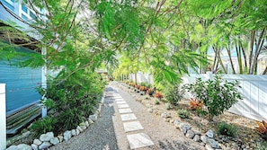 Ein Gartenpfad mit trittfesten Steinen, umgeben von unterschiedlichen Pflanzen und einem weißen Zaun.