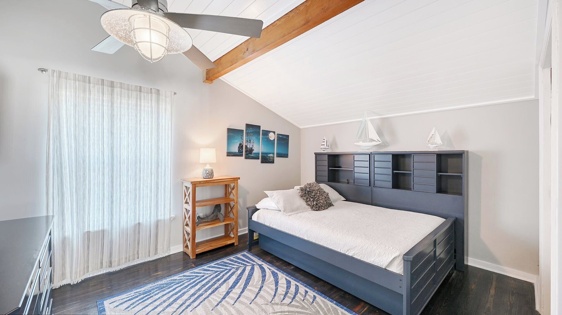 A bedroom with a bed, a nightstand, a ceiling fan, and artwork on the wall.
