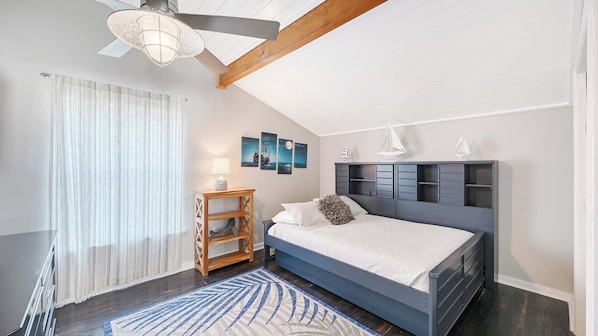 Ein Schlafzimmer mit einem Bett, einem Nachttisch, einem Deckenventilator und Kunstwerken an der Wand.