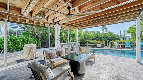 An outdoor patio with a pool, covered seating area, and a ceiling fan.