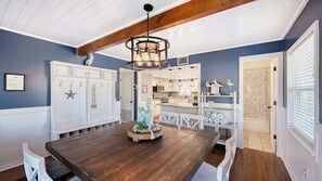 A dining area with a wooden table, white chairs, a decorative centerpiece, and a kitchen in the background.