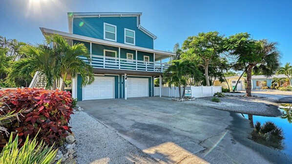 A two-story house with a blue exterior, a front garage, and a small driveway. - Stunning 3Bed/3 Bath, Heated Pool, FREE WiFi, Close to Beach, On Canal to Dock your Boat (Anna Maria)