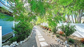 Un sendero en un jardín con piedras para pisar, rodeado de plantas variadas y una valla blanca.