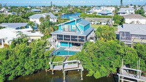 A modern house with a large pool, surrounded by lush greenery and a waterfront view. - Stunning 3Bed/3 Bath, Heated Pool, FREE WiFi, Close to Beach, On Canal to Dock your Boat (Anna Maria)
