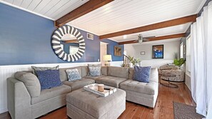Ein Wohnzimmer mit einem Ecksofa, einem runden Spiegel und einem Deckenventilator.