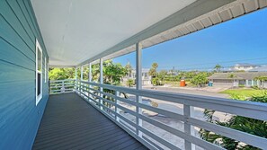A covered porch with a view of a residential area, including houses and greenery.