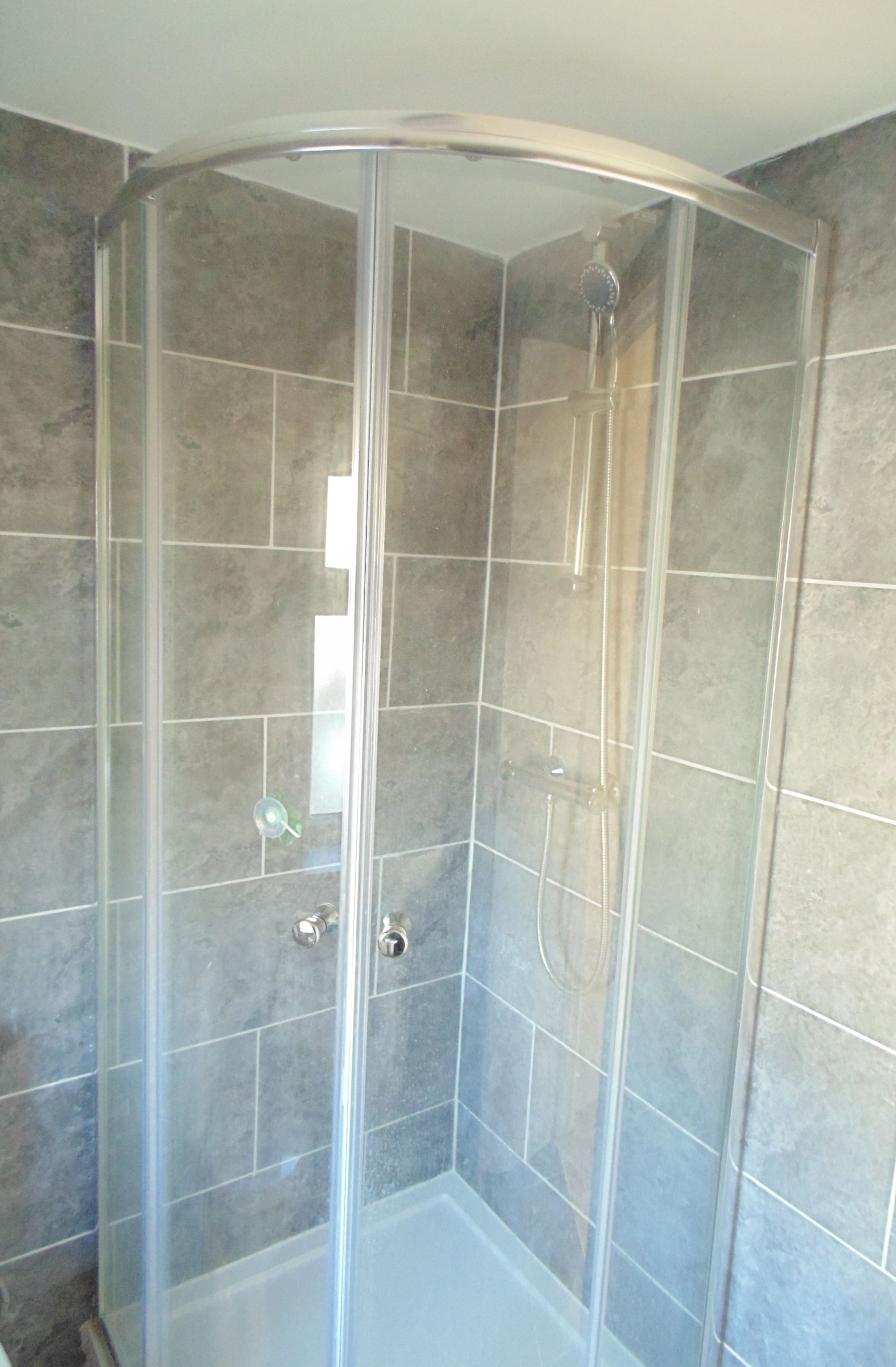 A glass-enclosed shower with a curved ceiling, tiled walls, and a visible showerhead.