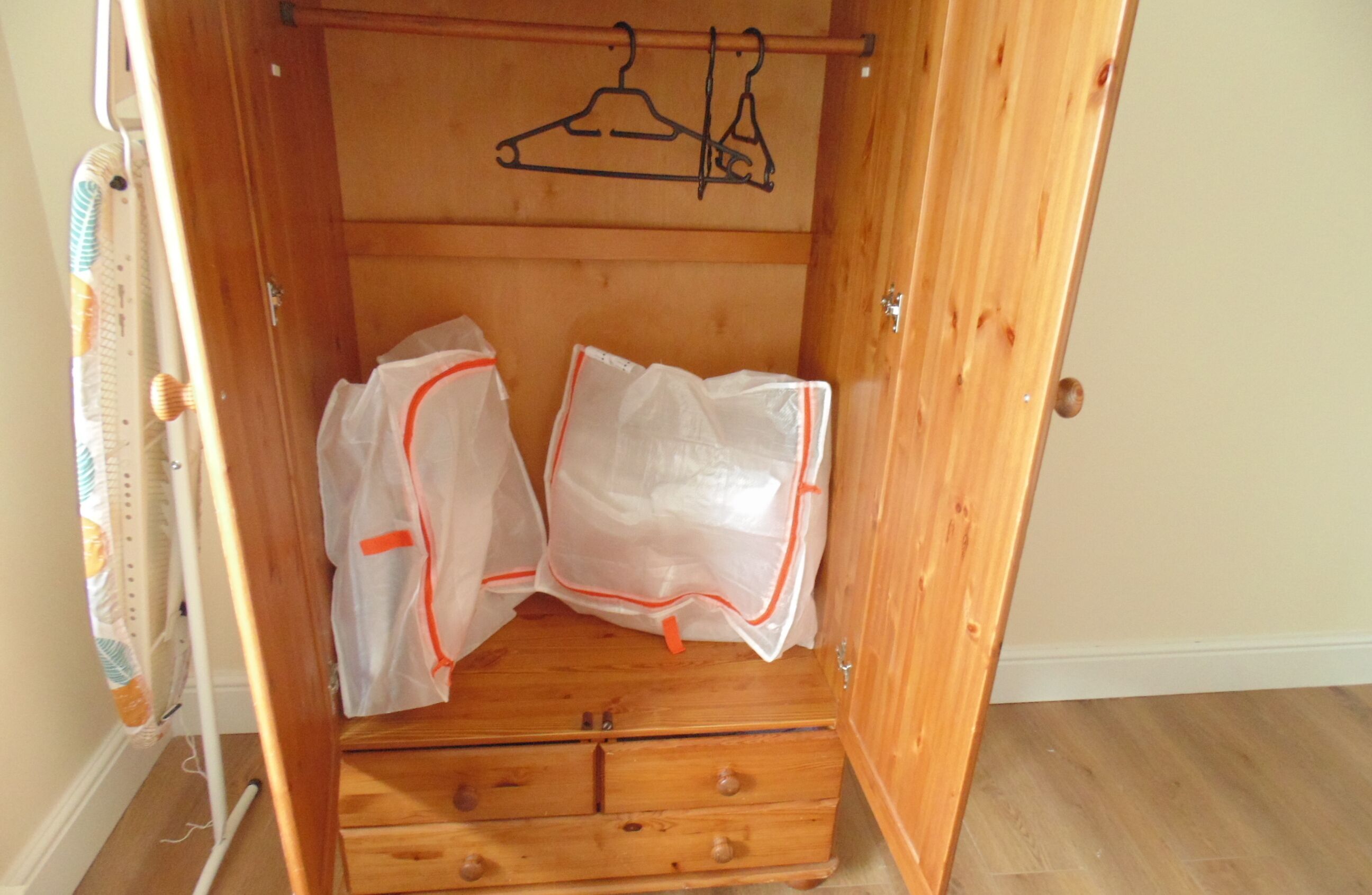 Een houten garderobe met twee doorzichtige plastic zakken aan de deur, een houten vloer en een houten deur met een simpele handgreep.