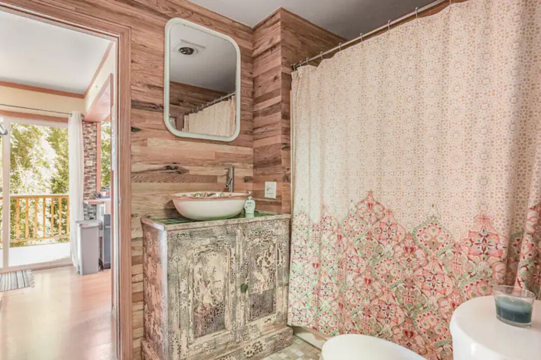 A bathroom with a wooden wall, a sink with a decorative basin, a mirror, and a shower curtain with a floral pattern.