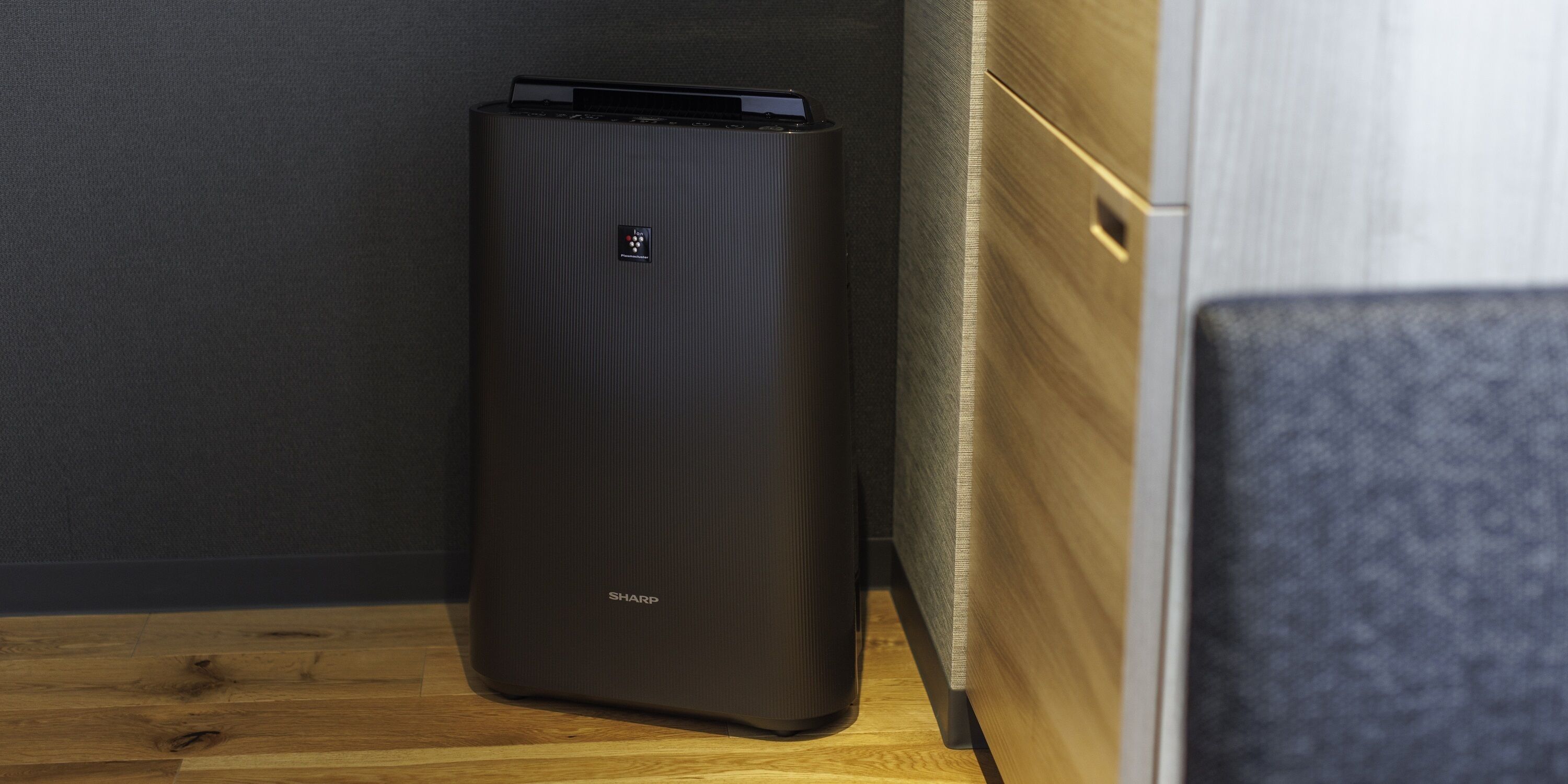 A black, ribbed, rectangular device with the brand name 'SHARP' on its side, placed on a wooden floor against a grey wall.