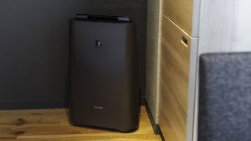 A black, ribbed, rectangular device with the brand name 'SHARP' on its side, placed on a wooden floor against a grey wall.