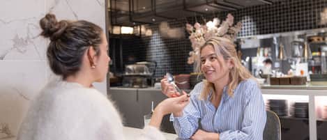 Dos personas cenando en un restaurante con una decoración moderna, paredes de mármol y una cocina a la vista.