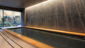 A modern indoor pool with a glass wall, a wooden deck, and a textured wall.