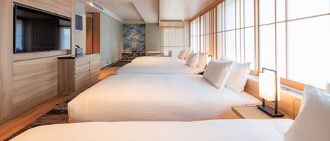 A hotel room with a large bed, a TV mounted on the wall, and a view of the city through large windows.