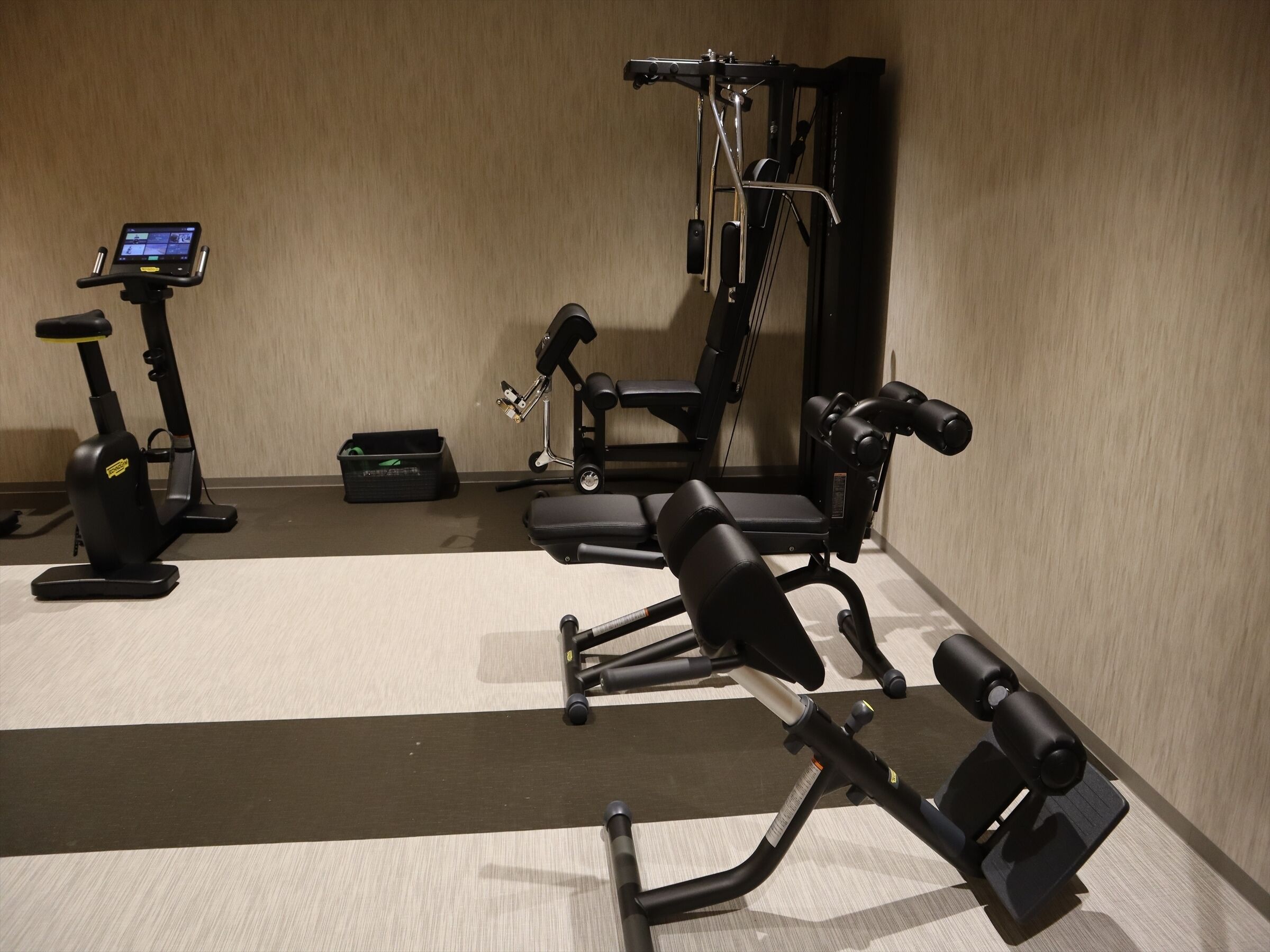 A gym with a stationary bike, a bench press, and a weight bench.