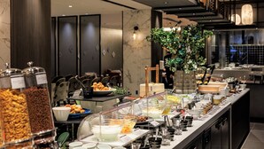 En buffet med forskellige madmuligheder, herunder en salatbar, samt et siddeområde med stole og en plante.