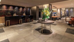 En moderne hotellobby med receptionsdisk, siddeområde og en dekorativ vase med blomster.