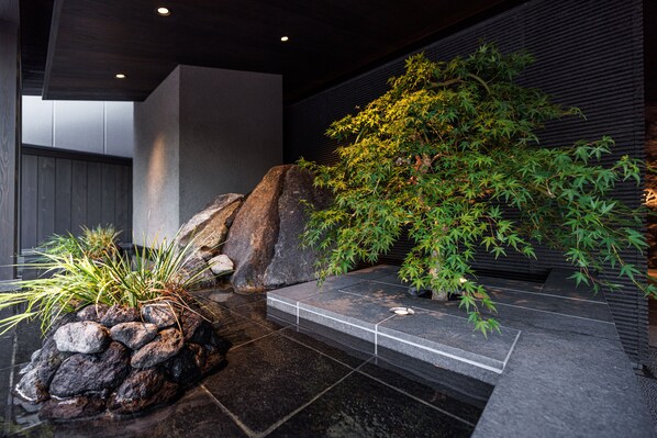 A modern indoor garden with a stone pathway, large rocks, and a variety of plants including a prominent bamboo tree.